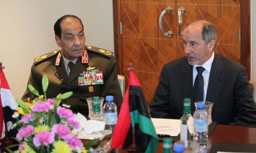 a man in uniform speaks next to another person