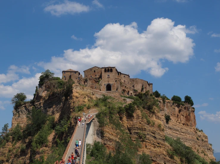 tourists on an outdoor walkway below a rock - covered castle