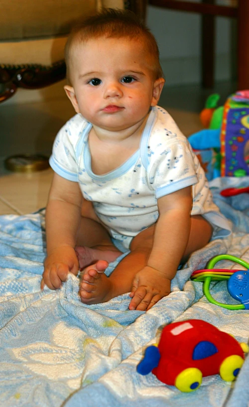 a baby wearing a t shirt sitting on a bed with toys