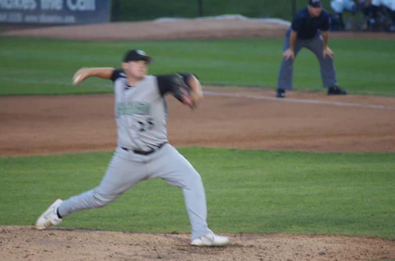 the baseball player is pitching a ball while the umpire watches