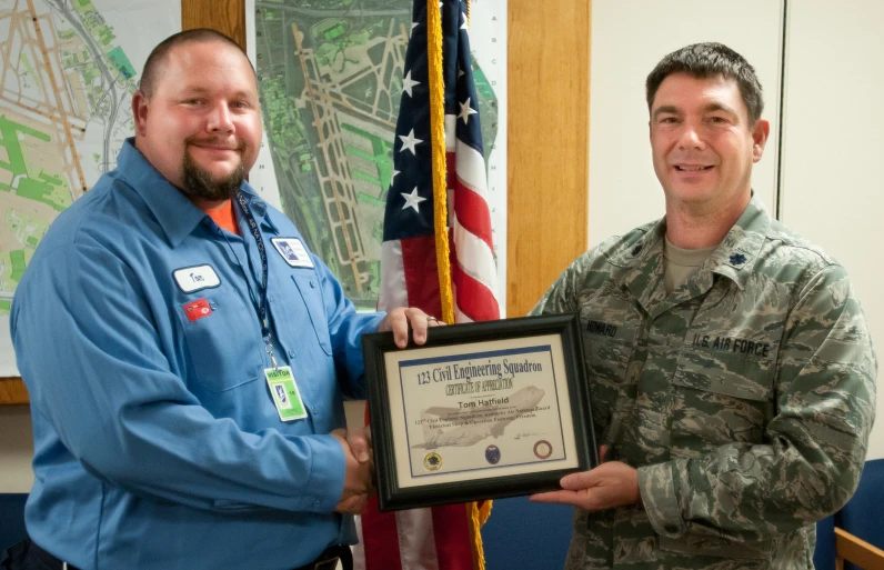 man presents plaque to fellow soldier in a camouflage uniform