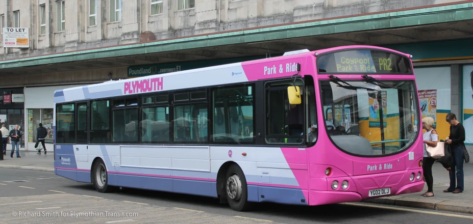 a pink, blue and white bus driving down the road