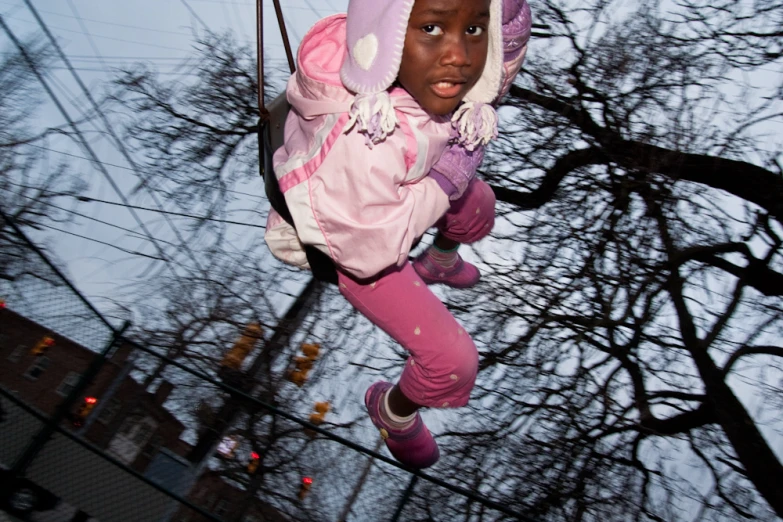 a child dressed in a pink jacket and hat swinging on a swing in the air