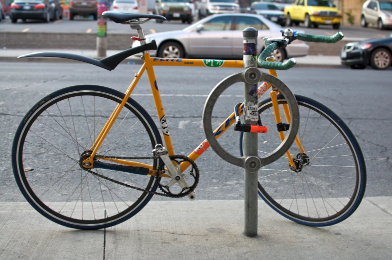 a bicycle sitting next to a pole with cars parked behind it