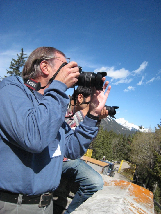 a man is sitting at the side of a hill while looking through his camera lens