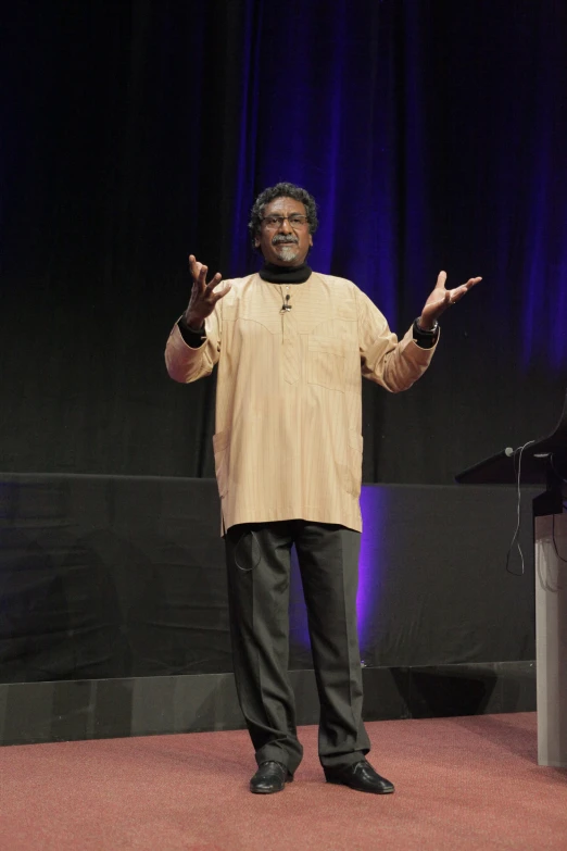 man in tan shirt with hands spread out in front of stage