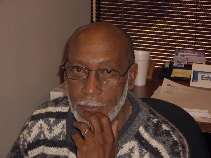 a man with glasses and a sweater is standing in an office