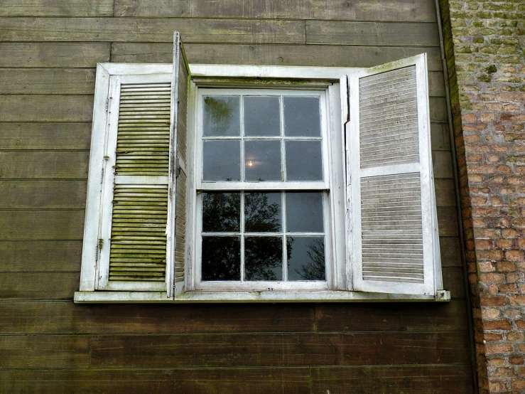 an old window with wooden shutters and tree leaves on the side of a building