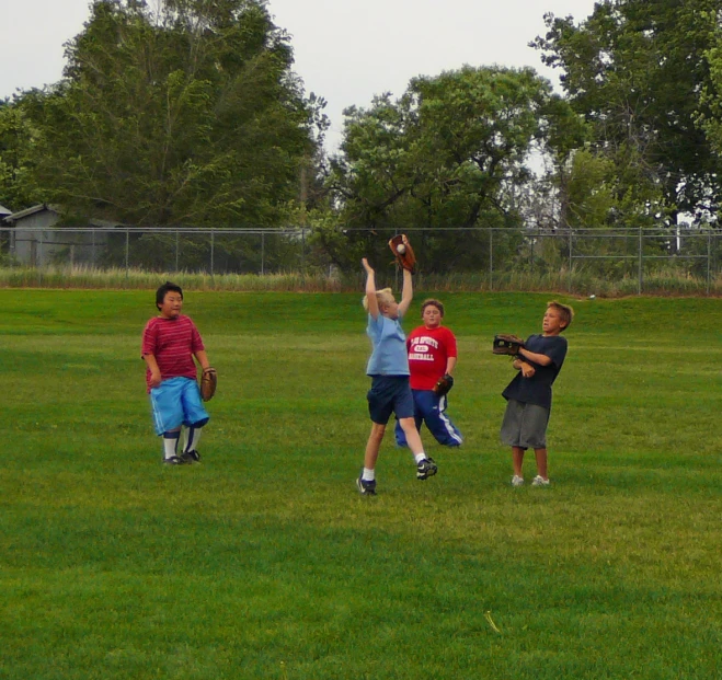 several young s in a grassy area holding up mitts