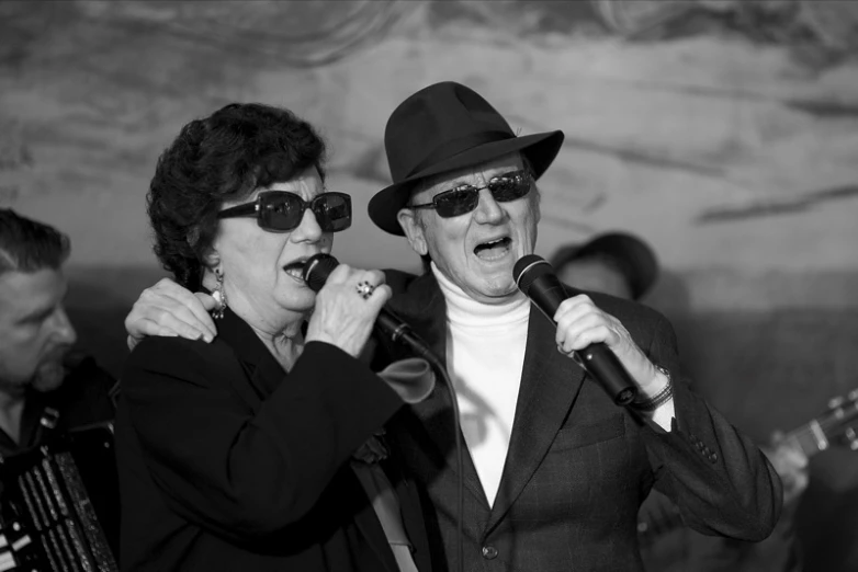 two people wearing sunglasses standing and singing