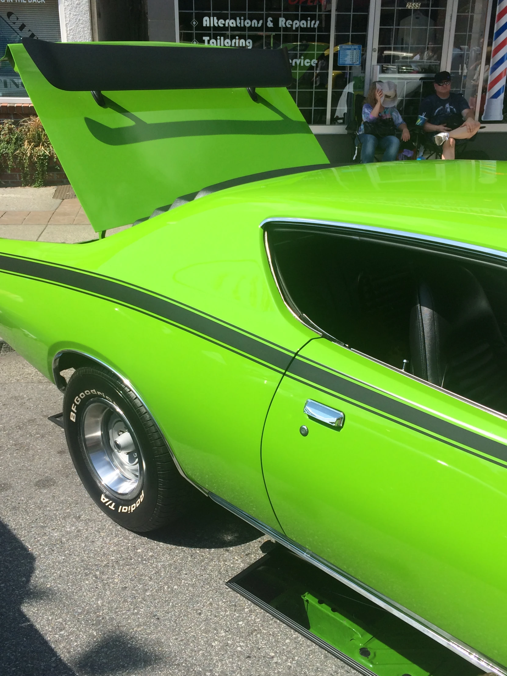 a green car with an open hood sitting outside a business