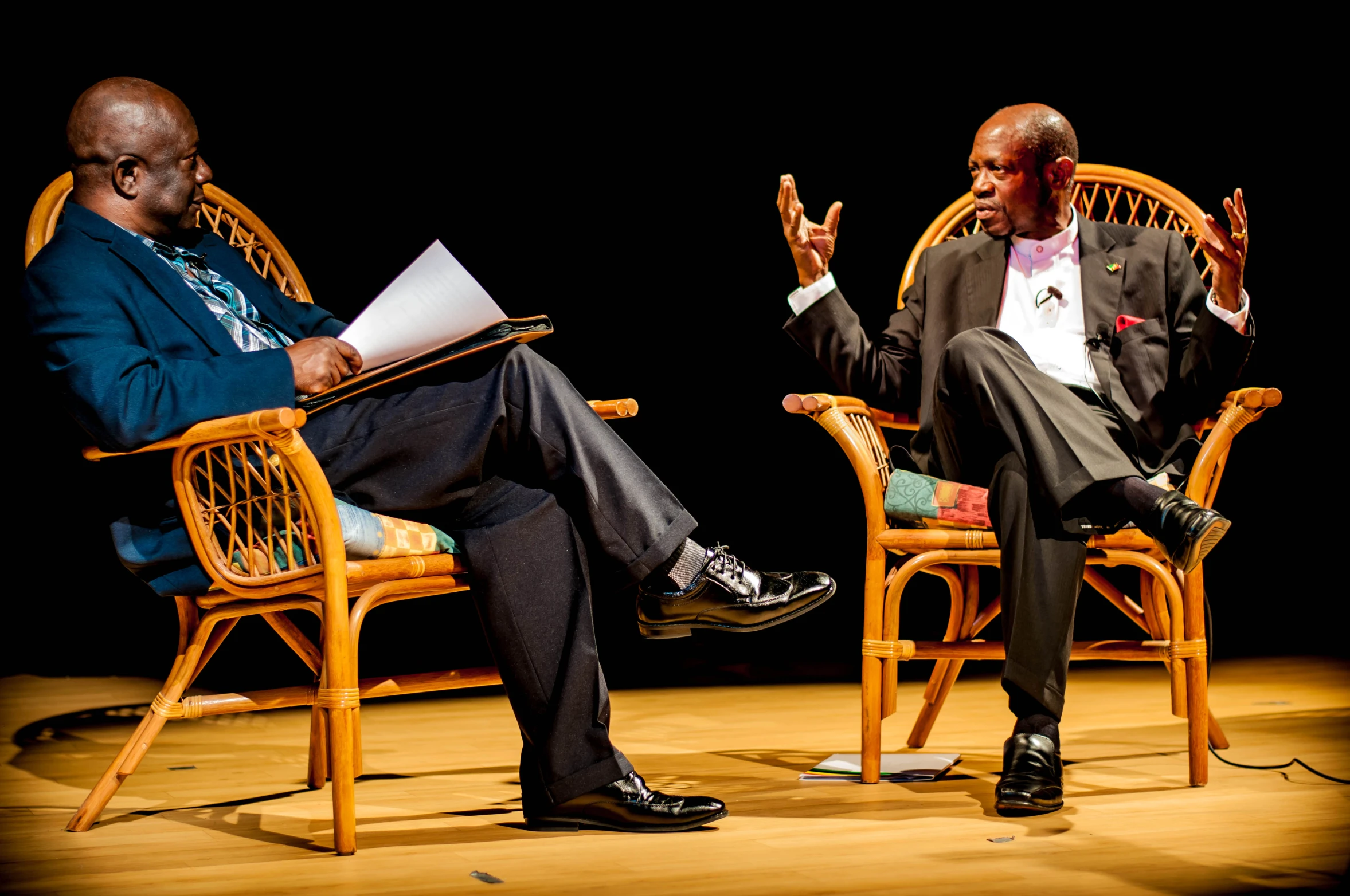 two men in chairs with one holding up the middle of his hand