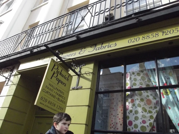 a little boy standing outside of a storefront with a window