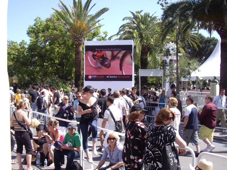 crowd of people standing in front of billboard on sunny day