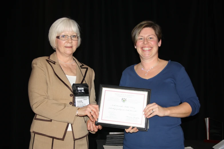 two women who are holding an award for work