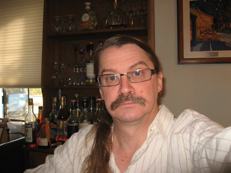man with glasses and mustache in front of wine glass cabinets