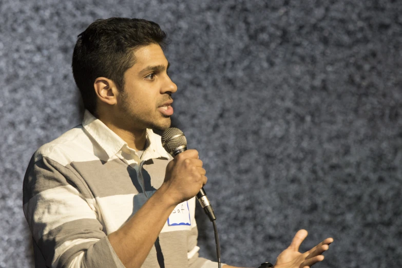 man standing behind a microphone holding his hands out and talking