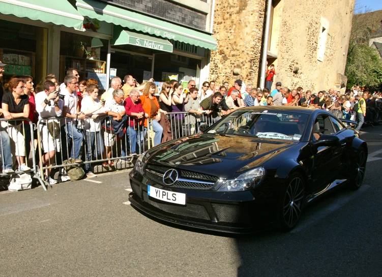 a black car driving down the street next to a crowd