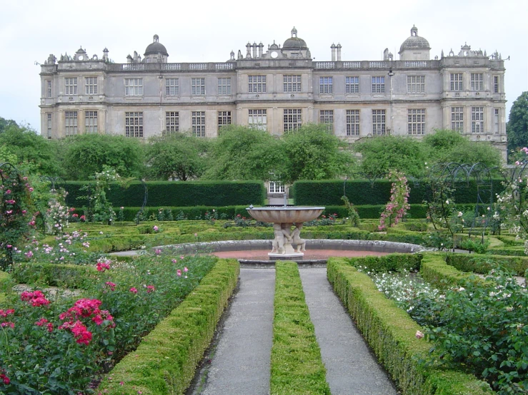 a garden with lots of plants and water fountain in front of a large building