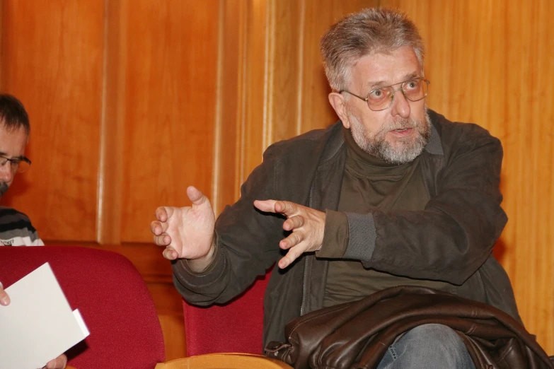 two men sitting in chairs talking and pointing at papers