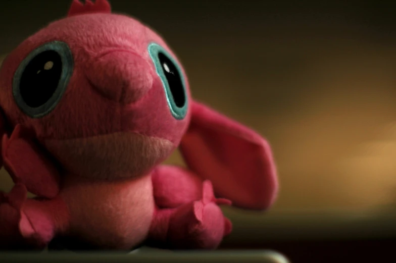 a pink stuffed toy with huge eyes on a shelf