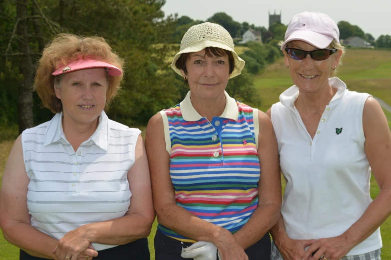 three women in hats and white shirts are holding golf bats