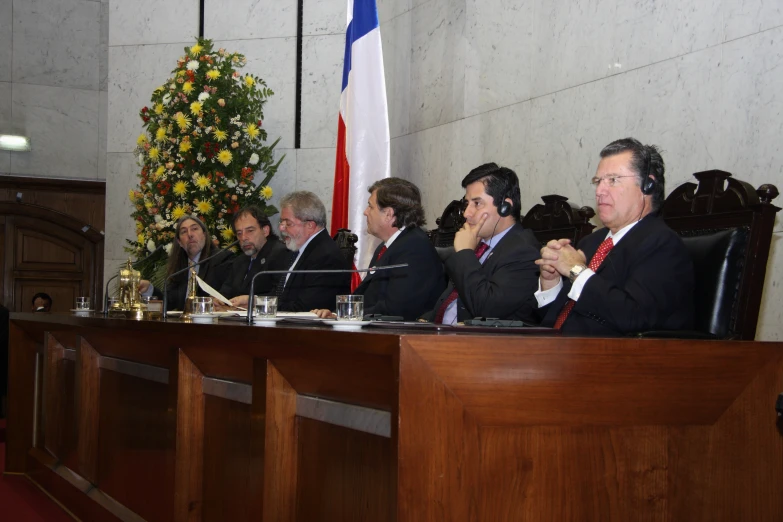 a group of men in business suits sit behind a long wooden desk