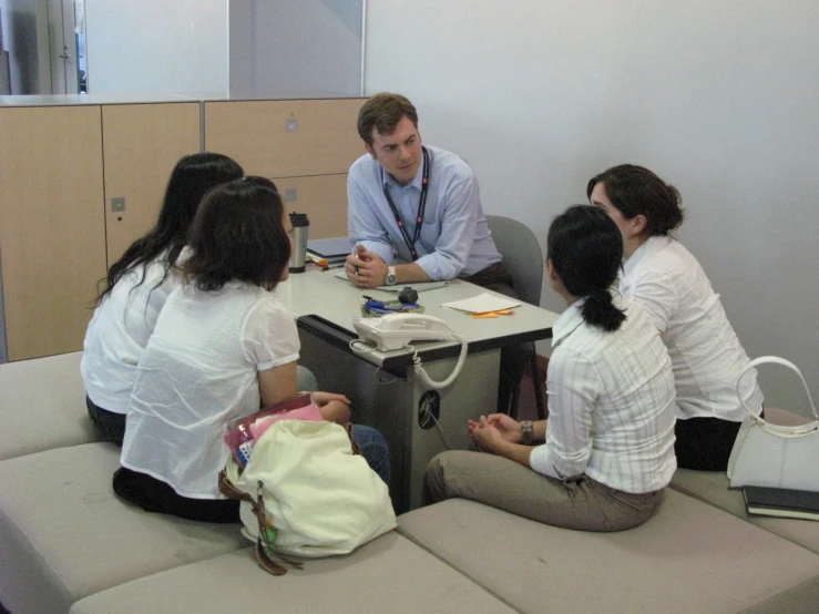 five people sitting around a table with a small laptop