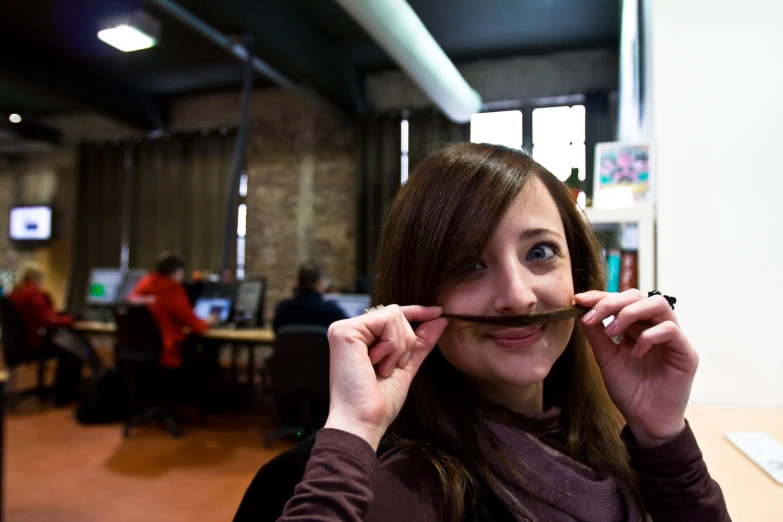 a girl smiles while holding a fake moustache on her nose