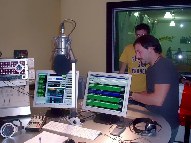 three people sitting at a desk with multiple monitors