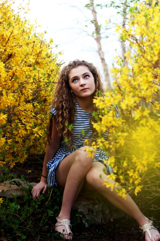 a girl sitting on a stone wall next to yellow flowers