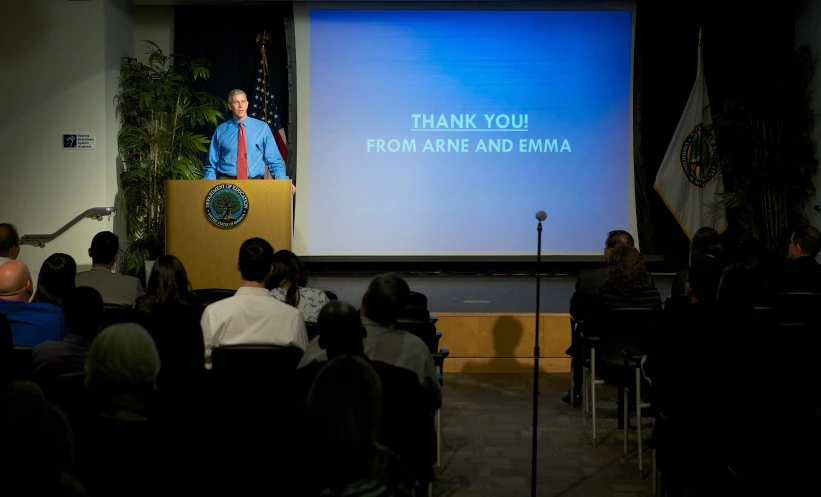 a man giving a speech to people in front of a large screen
