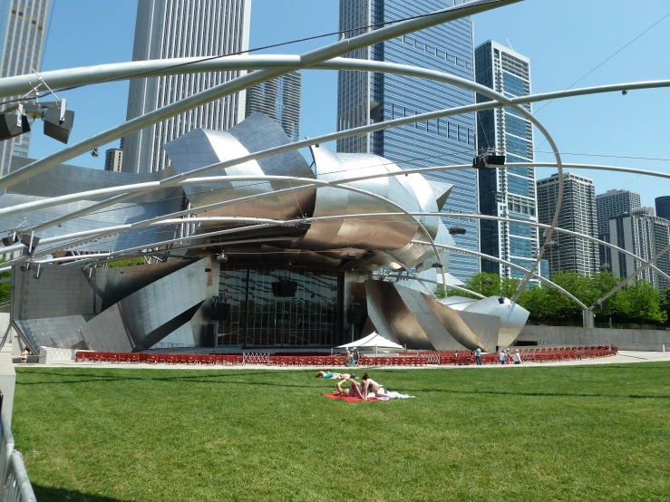 people sitting and laying in the grass near a large sculpture