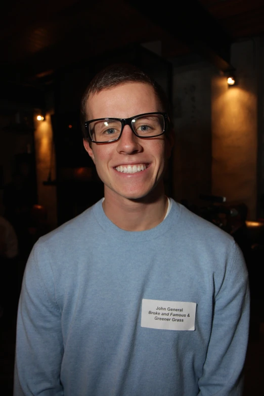 a smiling boy with dark glasses and a light blue sweater