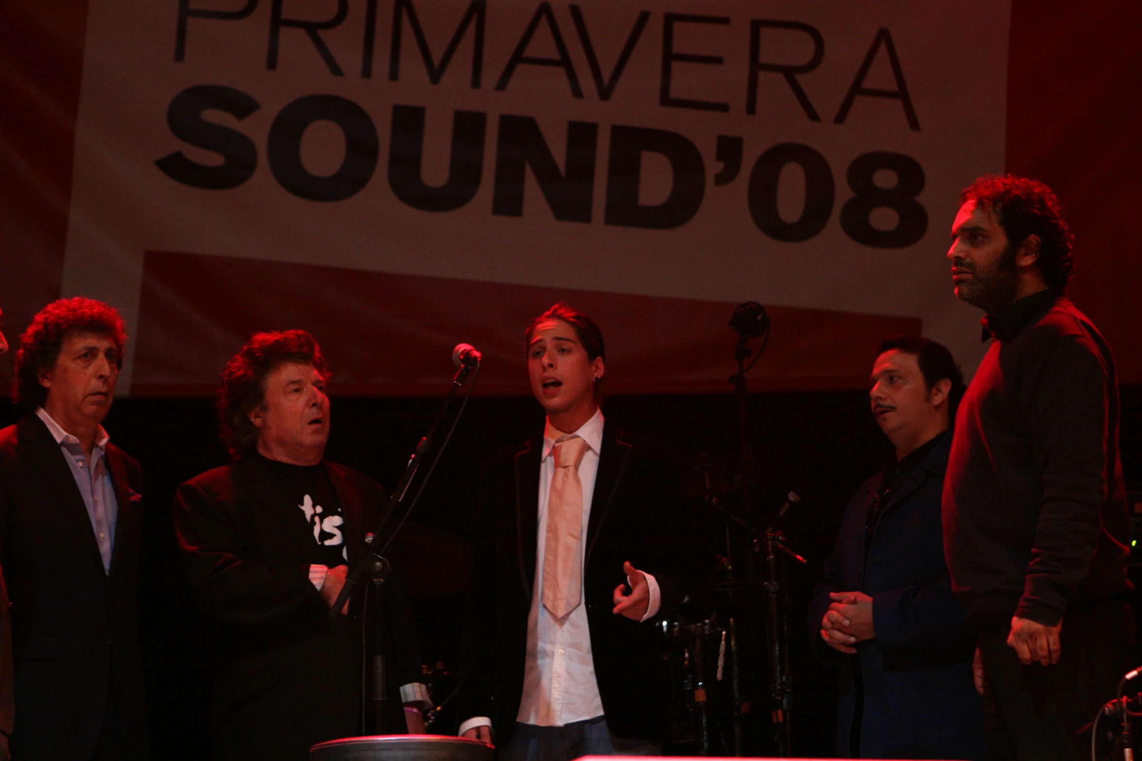 four people in front of a microphone on stage with sound 08 behind them