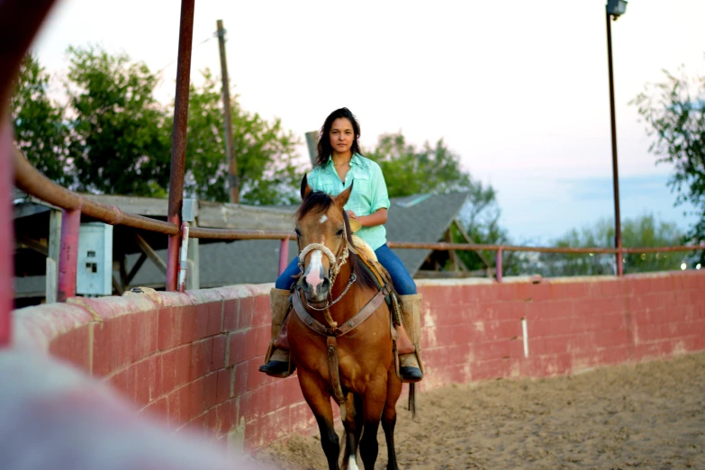 a woman riding a brown horse next to a fence