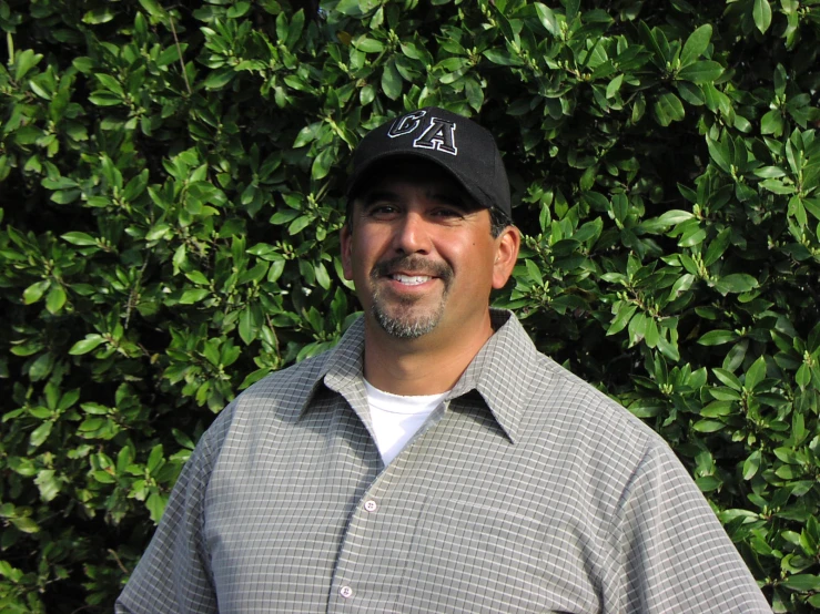 a man in front of a bush with a hat on