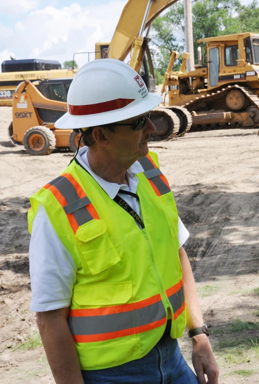 man with hard hat and safety vest in front of backhoes