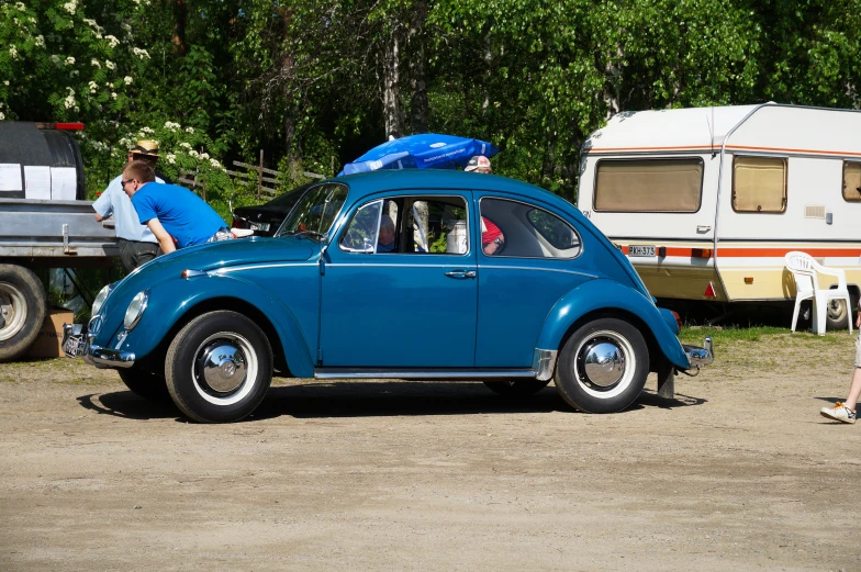 an old vw bug sits in a yard with people looking at it