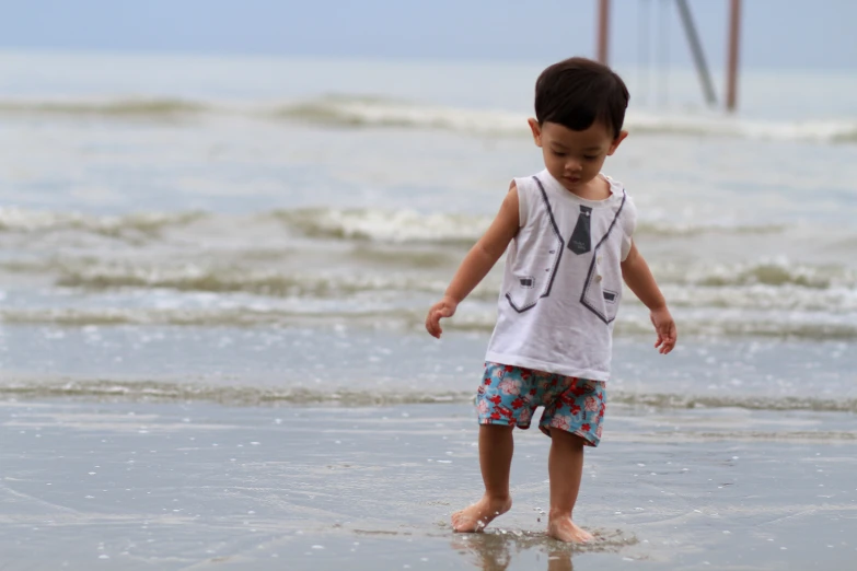 a little boy standing on the sand at the beach