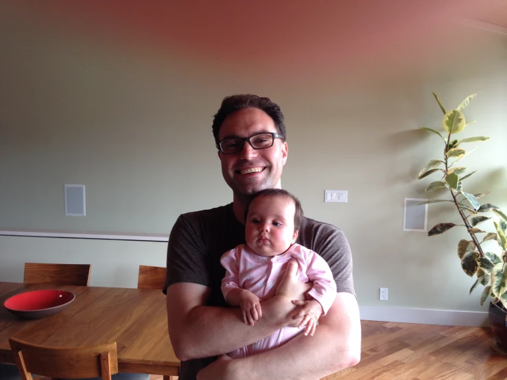 man with glasses sitting on a table holding a baby