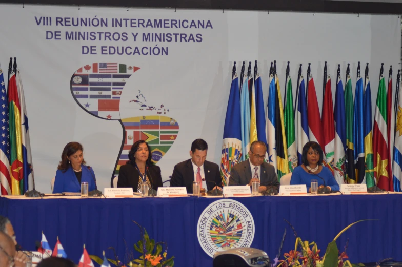 a group of people are gathered in front of two men and women at a table