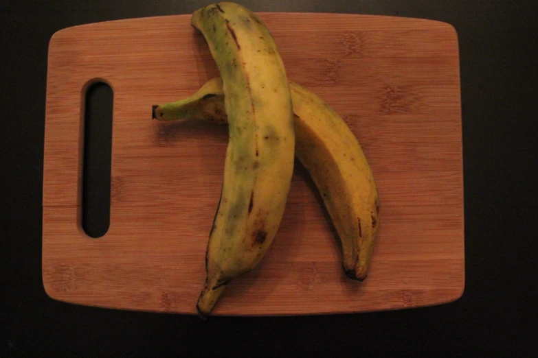 two bananas sit next to each other on a wooden  board