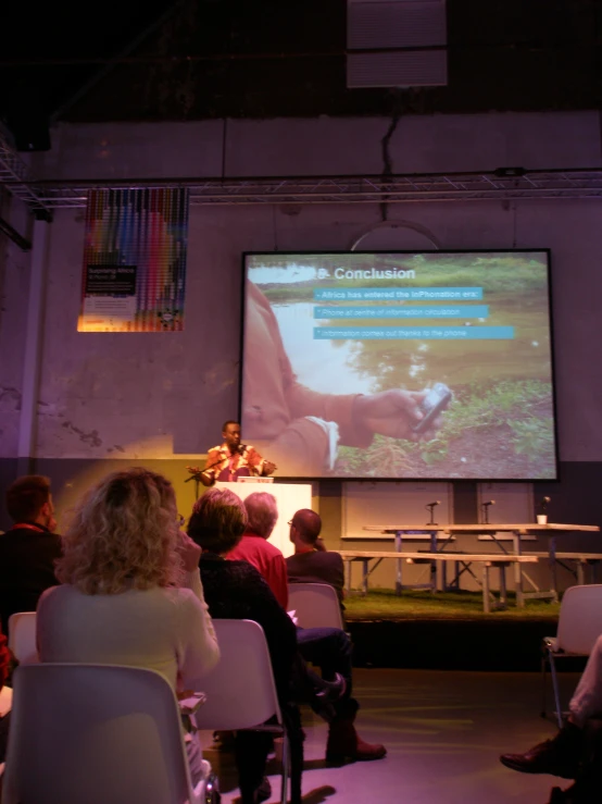 audience looking on screen with information displayed at stage