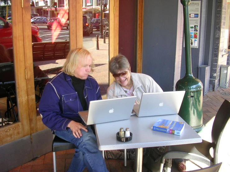 two women sitting at an outdoor cafe in front of computers