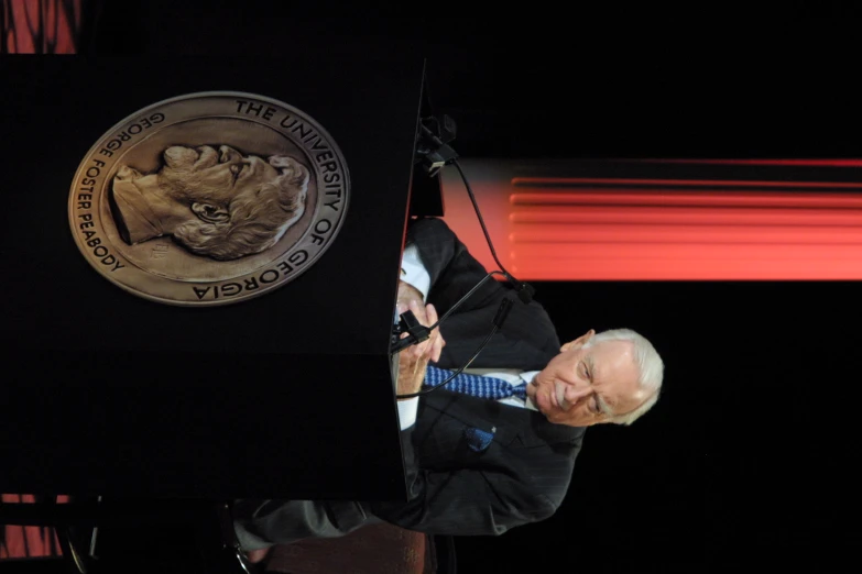 man with microphone in front of large lion plaque