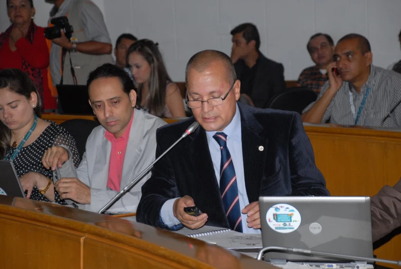 man sitting at a podium looking at his cell phone