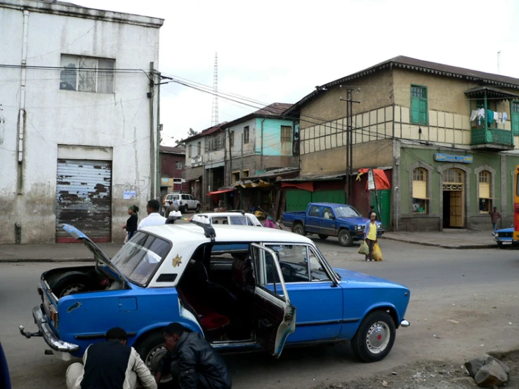 a blue car with open hood sitting on the street