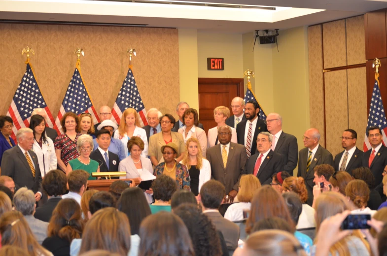 several people standing behind a podium in a room filled with flags