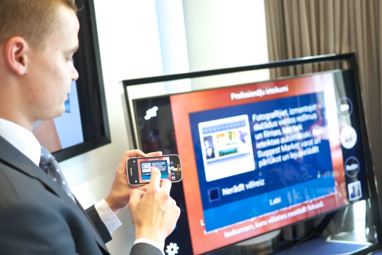 man looking at a large television with his phone in his hand